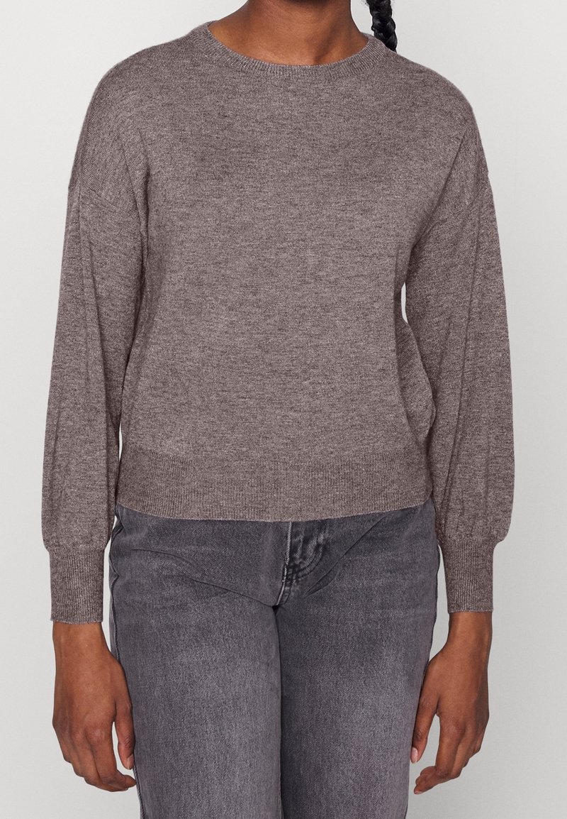 Brauner Strickpullover mit langen Ärmeln, rundem Halsausschnitt und geripptem Saum. Kombiniert mit grauen Jeans aus Denim. Weiche Textur und lockerer Schnitt.