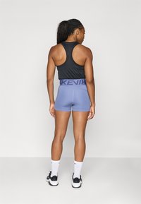 Czarny bezrękawnik z plecami w stylu racerback, w zestawieniu z jasnofioletowymi szortami o wysokim pasie z logo "NIKE".