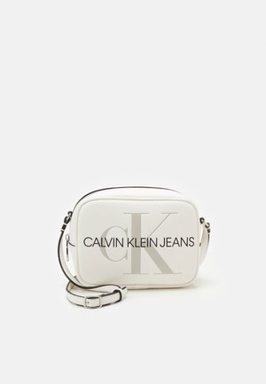 Biała torba crossbody z czarnym napisem „CALVIN KLEIN JEANS” i dużym logo „CK”. Gładkie wykończenie, zamek błyskawiczny, regulowany pasek.