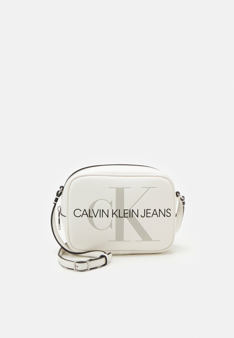Biała torba crossbody z czarnym napisem „CALVIN KLEIN JEANS” i dużym logo „CK”. Gładkie wykończenie, zamek błyskawiczny, regulowany pasek.