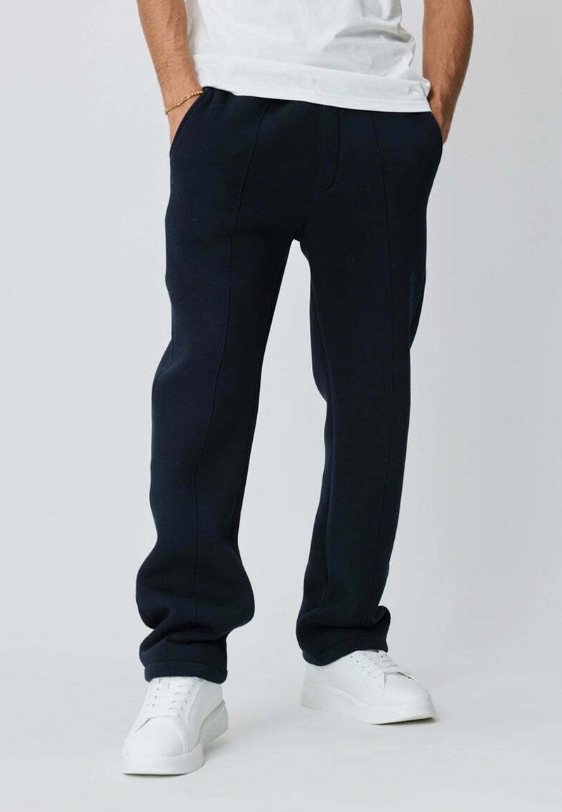 Pantalons de jogging bleu marine en tissu doux, avec poches latérales et design de jambe fuselée, associés à des baskets blanches.