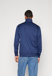 Marinblåzip-jacka med hög krage, lång ärm och elastisk nederdel, tillverkad av ett mjukt material, i kombination med ljusblå jeans.