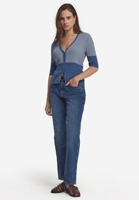 Blå ribbad cardigan med korta ärmar och djup V-ringning, med mörkare och ljusare blå sektioner. I kombination med högmidjade denimjeans.