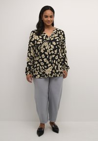 Blouse noire avec motif floral blanc, encolure en V, manches longues, associée à un pantalon large gris clair et des ballerines noires à bout pointu.