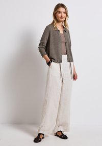 Šedý button-up svetr, béžový top na ramínka, krémové široké kalhoty, černé tkané sandály. Měkké materiály a volnější střih vytvářejí ležérní vzhled.
