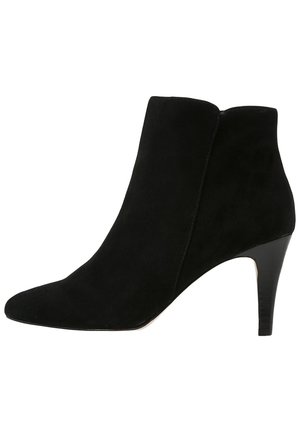 Sort ankelstøvle i ruskind med spids tå og slank høj hæl, lynlås i siden, minimalistisk design.