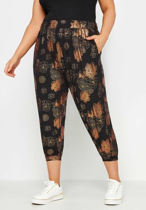 Pantalons noirs à taille élastique avec des motifs floraux bruns, longueur cropped, poches latérales et poignets froncés. Associés à des baskets blanches.