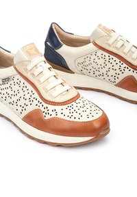 Zapatillas de cuero con parte superior en color crema, acentos marrones y parte trasera en azul marino. Presentan un diseño perforado, cordones blancos y suela de goma texturizada.