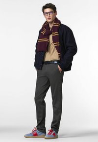 Donkerblauwe bomberjack, beige trui, grijze broek, maroon en gouden gestreepte sjaal, blauw en rode sneakers met textuurdetails.