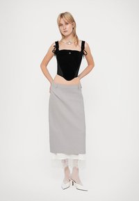 Μαύρος βελούδινος κορσές με ρυθμιζόμενους ιμάντες ώμου, συνδυασμένος με γκρι φούστα με δαντελένια λεπτομέρεια. Λευκά ψηλοτάκουνα παπούτσια ολοκληρώνουν την εμφάνιση.