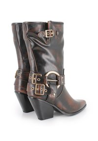 Botas de tobillo de cuero marrón con un acabado brillante, que presentan herrajes en tono dorado, un gran anillo metálico y dos correas ajustables.