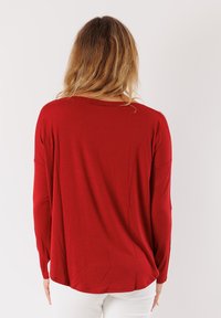 Maglia rossa a maniche lunghe realizzata in tessuto morbido e elasticizzato; presenta un collo rotondo e una vestibilità morbida con spalle scese. Texture liscia.