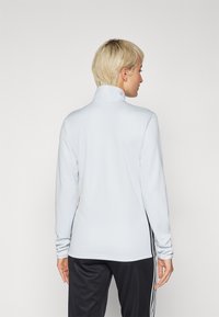 Light blue long-sleeve pullover with a standing collar, smooth texture, and black side accents. Worn with black pants featuring stripes.