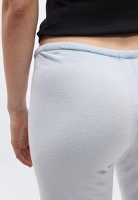 Κοντινό πλάνο ενός ατόμου που φοράει γαλάζια πλεκτή παντελόνα και μαύρο κοντό τοπ, με εμφανή την κάτω πλάτη και το αριστερό χέρι σε λευκό φόντο.