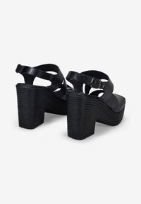 Sandalias de cuña negras con plataforma texturizada, correa ajustable y diseño recortado. Material de piel suave con tacón apilado.