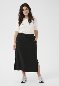 Fustă maxi neagră cu talie elastică, închidere cu șnur, slituri laterale și două buzunare frontale. Asortată cu un tricou alb ajustat și adidași.