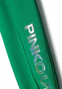 Gröna sweatpants med stort "PINK"-tryck i glänsande, iriserande material prytt med rhinstenar längs sömmen. Mjuk tygtextur.