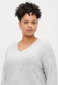 Sweater cinza de malha com decote em V, apresentando um acabamento suave e texturizado e mangas largas. Material leve e suave.