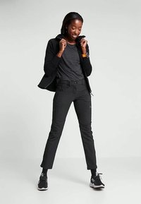 Čierna mikina a šedé tričko v kombinácii s úzkymi čiernymi nohavicami. Tenisky majú čierno-biele akcenty. Model stojí na neutrálnom pozadí.