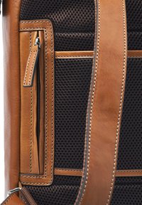 Close-up of brown leather backpack strap and small zippered pocket on black mesh fabric panel.