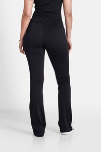Pantalons évasés noirs texturés avec une taille cintrée, présentant un motif en relief subtil et une finition lisse. Associés à des baskets blanches.