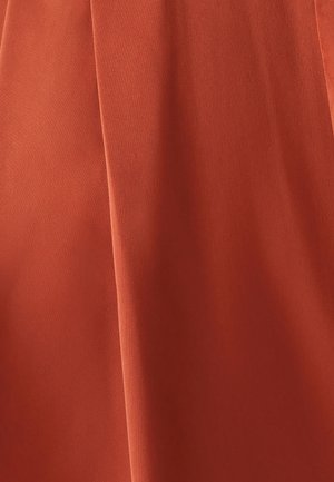 Hrdzavooranžová látka sa jemne vlní s hladkým povrchom, pričom má jemné záhyby a matný povrch, čo naznačuje ľahký materiál.