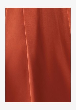 Rostorange Stoff liegt sanft mit einer glatten Textur, zeigt subtile Falten und hat ein mattes Finish, was auf ein leichtes Material hinweist.