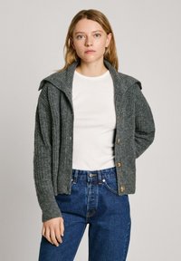 Grå ribbad cardigan med huva, träknappar och långa ärmar, bärs över en vit skjorta och kombineras med blå denimjeans.