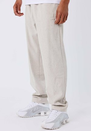 Joggers de color gris claro, texturizados y con un sutil patrón moteado, que cuentan con bolsillos laterales y un logo bordado en el muslo.
