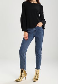 Top nero a maniche lunghe con un fit rilassato, abbinato a jeans blu a vita alta e stivaletti metallici dorati con punta affusolata.