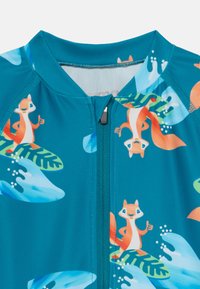 Rashguard de nage teal avec des graphiques de écureuils de dessin animé, des feuilles tropicales et des vagues éclaboussantes ; comprend une fermeture éclair à l'avant et une texture lisse.