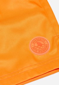 Ryškiai oranžiniai maudymosi šortai, pagaminti iš lygaus audinio, su apvaliu, iškilniu logotipo ženklu šviesesnėje oranžinėje spalvoje.