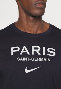 Granatowy bawełniany t-shirt z dużym białym napisem "PARIS SAINT-GERMAIN" i białym logo Nike z przodu. Okrągły dekolt, krótkie rękawy.