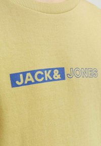 Felpa gialla in cotone con scollo rotondo. La parte anteriore presenta la scritta blu: "JACK&" in grassetto e "JONES" in un carattere più leggero.