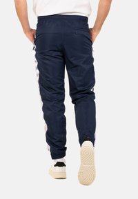 Marineblauwe trainingsbroek met elastische tailleband, zijpanelen in het wit en logo-accenten. Gemaakt van een gladde stof, voorzien van een ritszak.