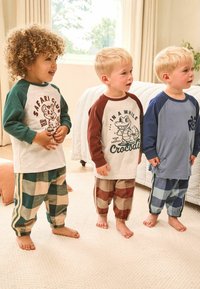 Tres niños llevan pijamas a juego. Las camisetas son de manga larga con estampados gráficos. Los pantalones tienen patrones de cuadros contrastantes en telas suaves.