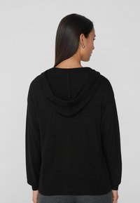 Czarny hoodie z długimi rękawami i prążkowanym hem. Miękka tekstura, luźny krój, cechujący się prostym designem i brakiem widocznych wzorów lub dodatków.