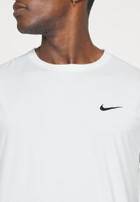 White Nike t-shirt with a round neckline, short sleeves, and a small black swoosh logo on the left chest. Smooth, lightweight fabric.