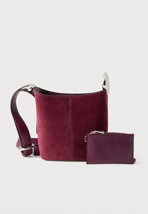 Bolso tipo cubo de ante burdeos con herrajes plateados y tarjetero a juego desmontable. Correa de cuero liso con detalles decorativos.