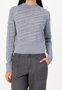 Pull en tricot bleu clair avec un motif texturé, encolure ronde et poignets côtelés. Associé à un pantalon cargo gris foncé avec poches latérales.