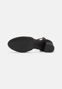 Black suede heel with a smooth, rounded toe and ankle strap. The bottom features a textured rubber sole for grip.