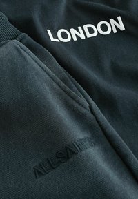 Tume roheline spordisärk, millel on valge "LONDON" kiri ja broderi "ALLSAINTS" logo. Pehme tekstuur koos soonikkoes varruka- ja alläärega.