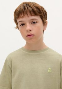 Lichtgroene katoenen t-shirt met een ruime pasvorm en korte mouwen, met een kleine, neon schedel en gekruiste botten accent op de borst.