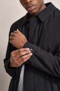 Schwarze Außenjacke mit einem strukturierten Kragen und Knopfmanschetten. Sie verfügt über eine glatte Stoffoberfläche und einen Reißverschluss auf der Vorderseite.