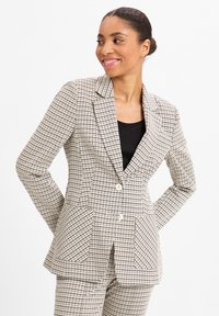 Beige karierter Blazer mit strukturierten Revers, zwei Taschen und einem Knopfverschluss, aus einem strukturierten Stoff in taillierter Passform.