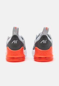 Chaussures de sport grises avec une tige en mesh, des accents orange et une semelle à coussin d'air visible. Elles disposent d'une languette et d'un logo "Air" en relief.