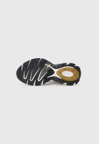 Black and white athletic shoe sole featuring a wavy tread pattern, dotted texture, and gold accent with brand logo.