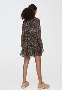 Robe fleurie avec un fond bleu marine, présentant de petites fleurs orange et bleues, une coupe ample et des manches longues. Tissu texturé et léger.