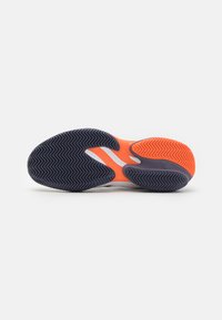 Såle av en sportsko, med et svart og oransje gummi-design som har et fiskebensmønster, buet form og strukturert overflate.
