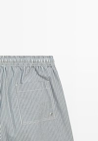 Modrá a bílá látka s vertikálními pruhy, elastickým pasem a čtvercovou zadní kapsou s viditelným stehem a malým kovovým nýtem.